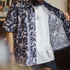 Person wearing a patterned shirt over a white t-shirt with a blurred background